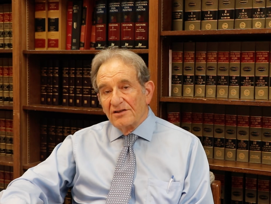 Attorney Jeff Stein seated in a law library, wearing a light blue shirt and patterned tie.